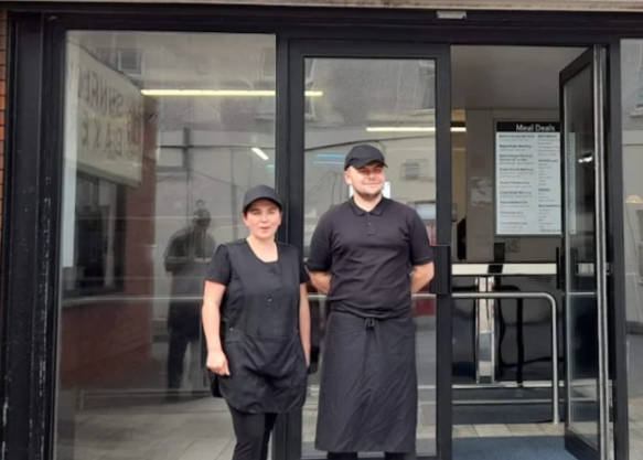 Two T & D Ford Fish and Chips staff members standing in the shop's front doorway.